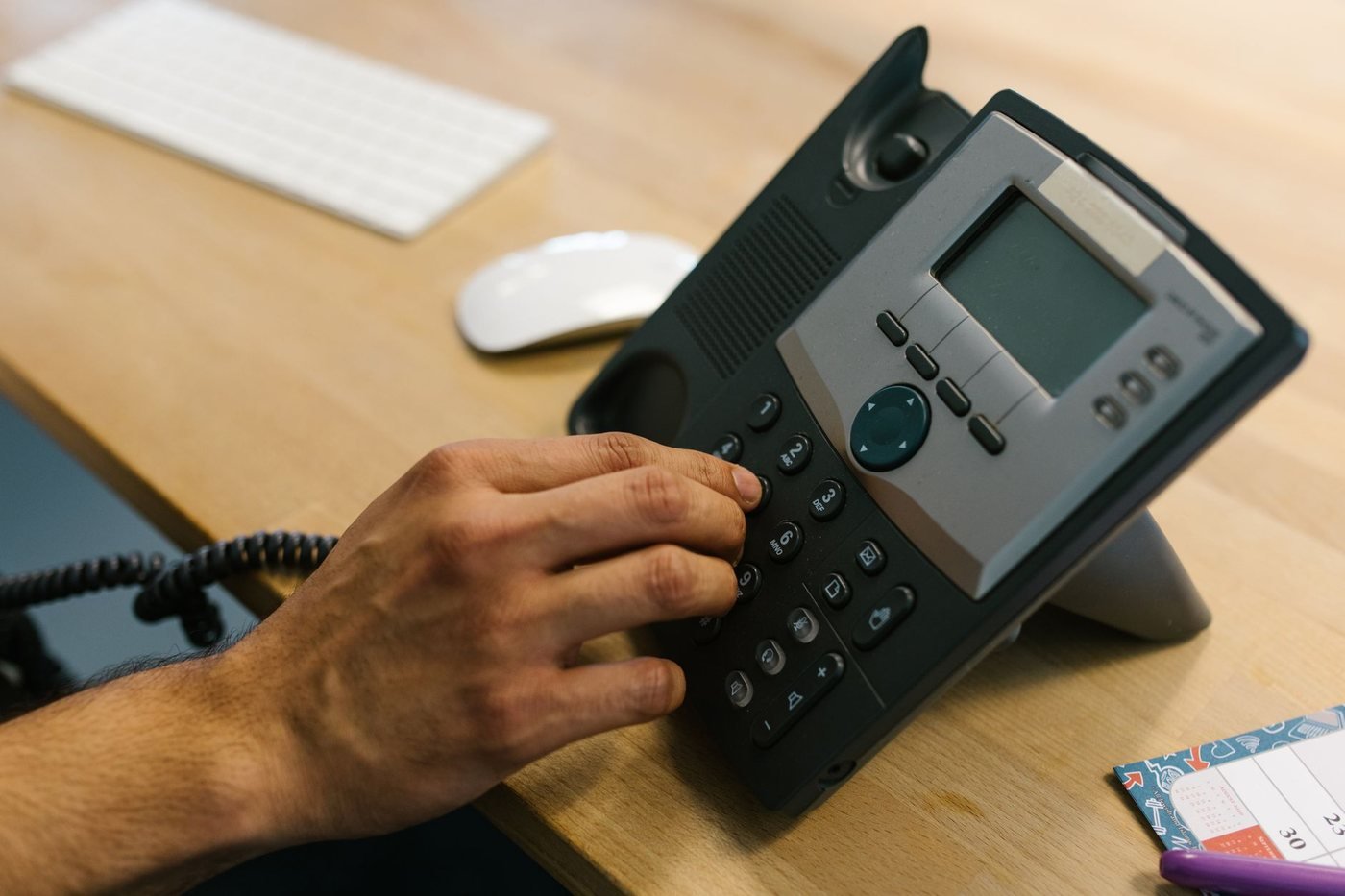 A hand lifting the handset of a desk telephone