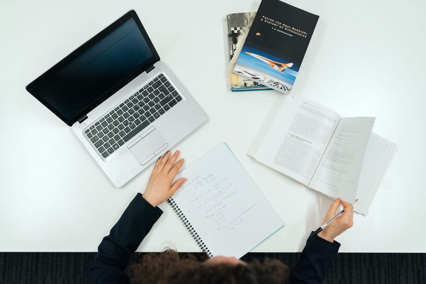 An overhead view of a desk with a laptop, open textbooks and handwritten notes